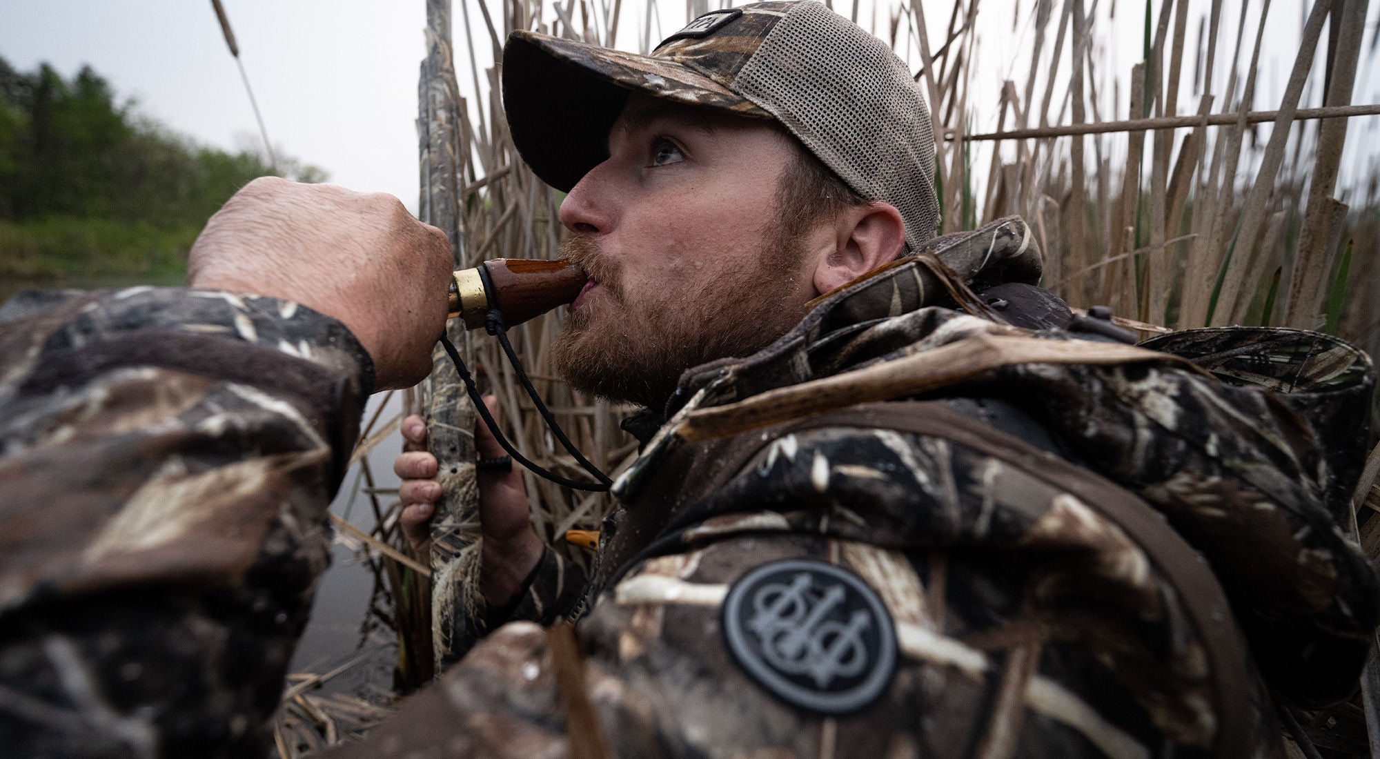 Camouflaged hunter using a duck call during waterfowl hunt.