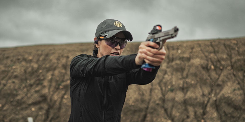 A woman in a black jacket and hat focusing on firearm training.