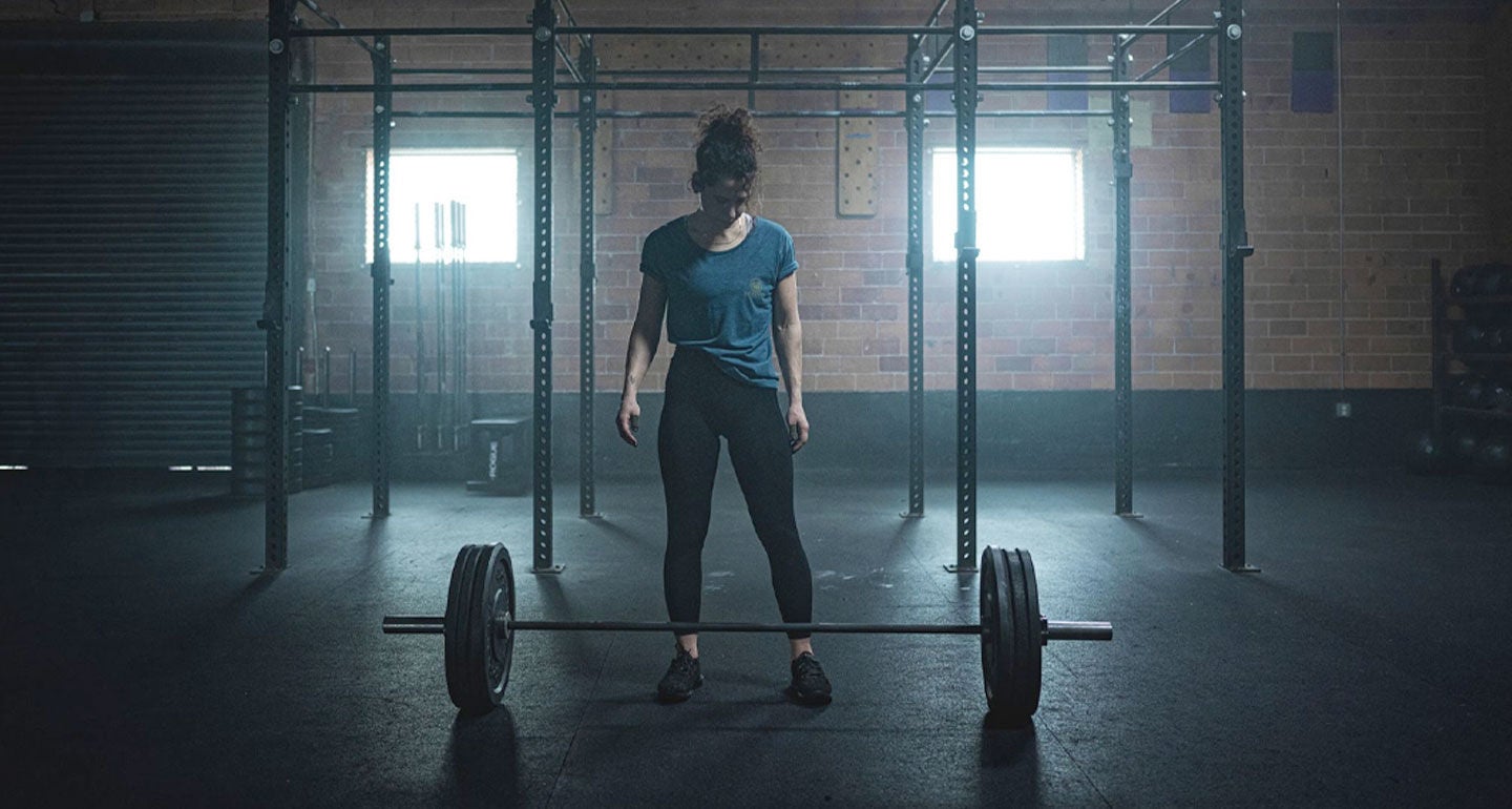 A woman stands in front of a barbell, preparing for physical training for concealed carry..